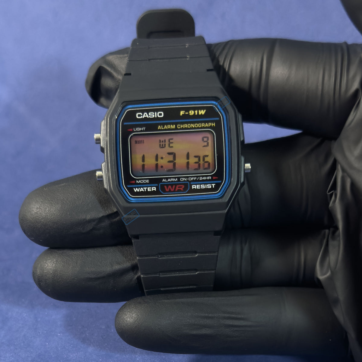Casio F-91W Sunset Horizont i svart handske, display i orange och rosa toner, från K-Project Lab