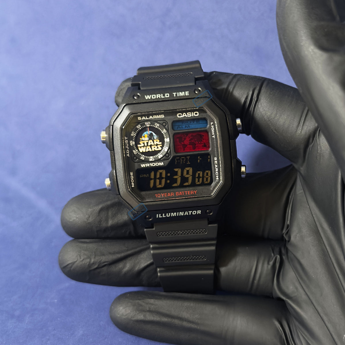 K-Project Labin muokkaama Casio AE-1200 Imperial Wars mustana hartsina mustassa hansikkaassa sinistä taustaa vasten