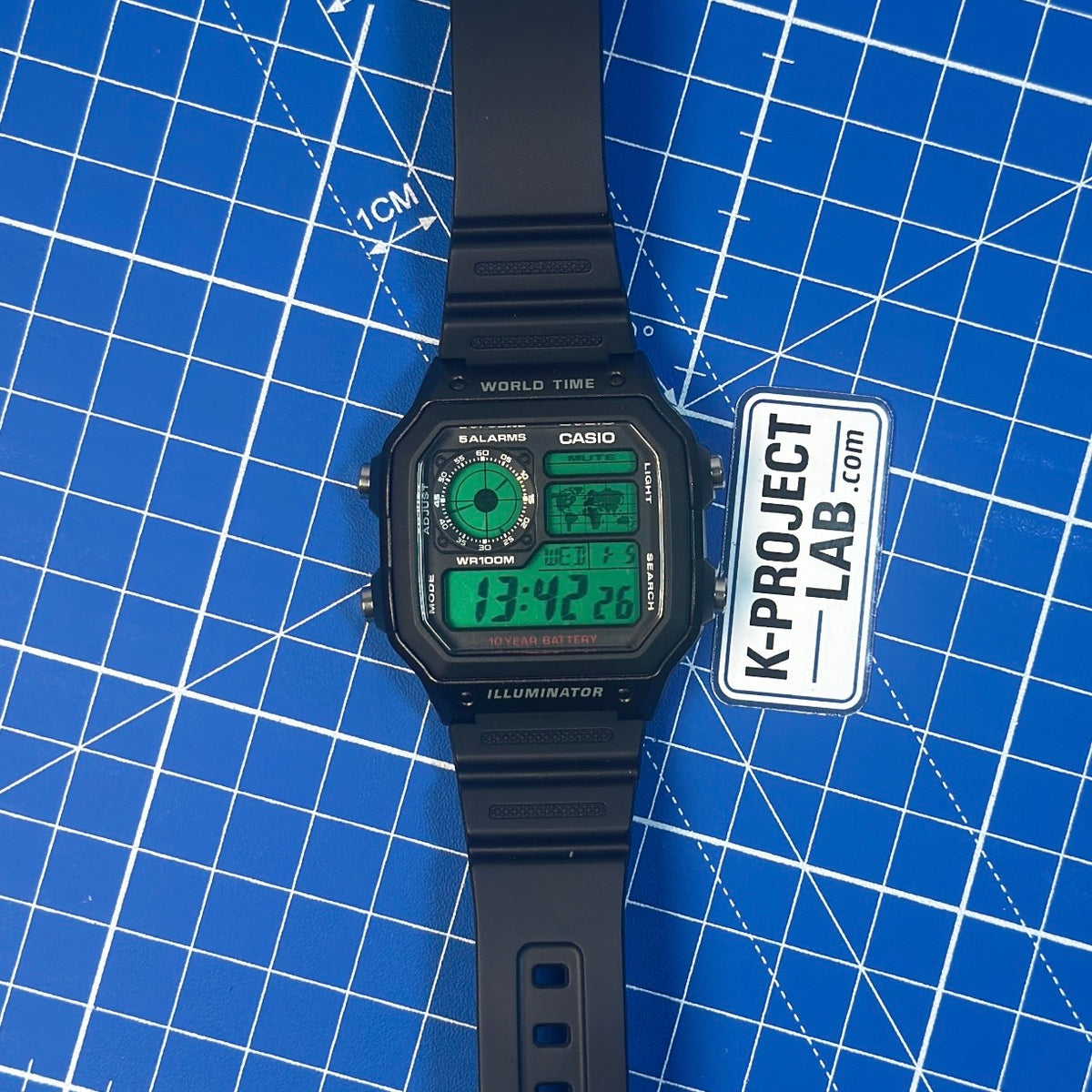 Casio AE-1200 Green Data Terminal mustana hartsina ranneke suorassa sinisellä pinnalla, K-Project Labilta