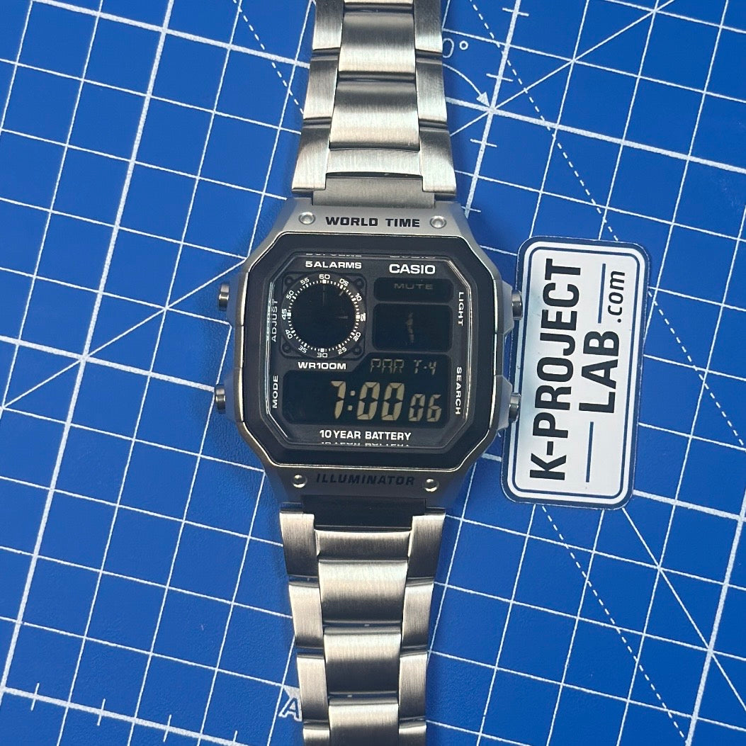 Casio AE-1200 Ghost in Stahl mit ausgelegtem Metallarmband auf der Werkstattmatte von K-Project Lab