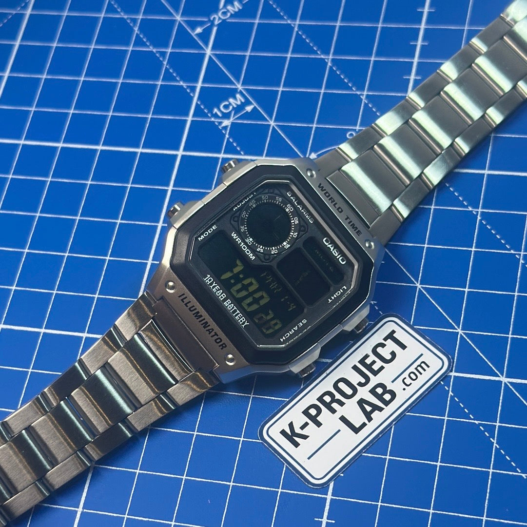 Casio AE-1200 Ghost in Stahl, schräg von der Seite auf blauer Matte, individualisiert von K-Project Lab