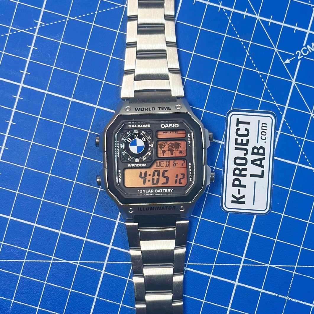 K-Project Labin Casio AE-1200 Midnight Bavarian teräksisenä, ylhäältä kuvattuna sinisellä taustalla