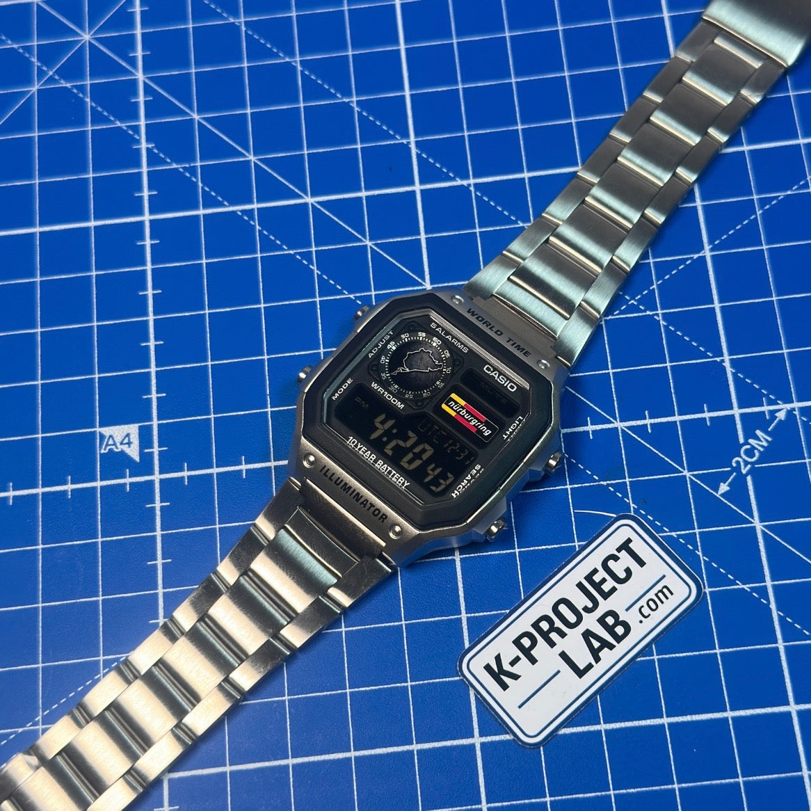 Casio AE-1200 Nordschleife Signal i stål snett framifrån på en blå arbetsmatta, från K-Project Lab