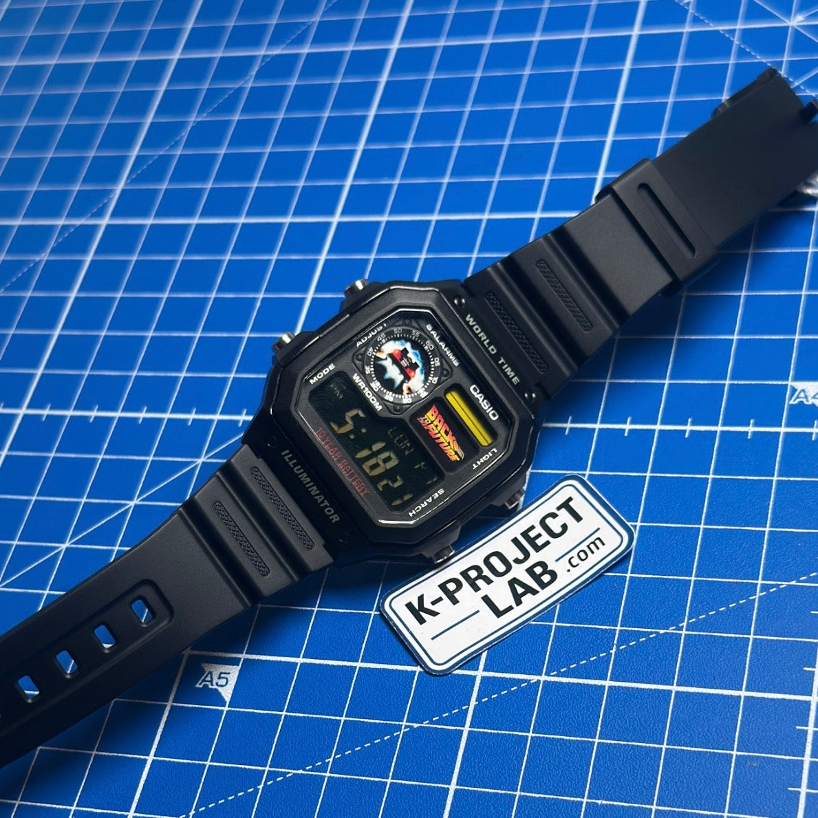 Casio AE-1200 Flux Horizon mustana hartsina viistosti, ranneke suorassa sinisellä taustalla, K-Project Labilta